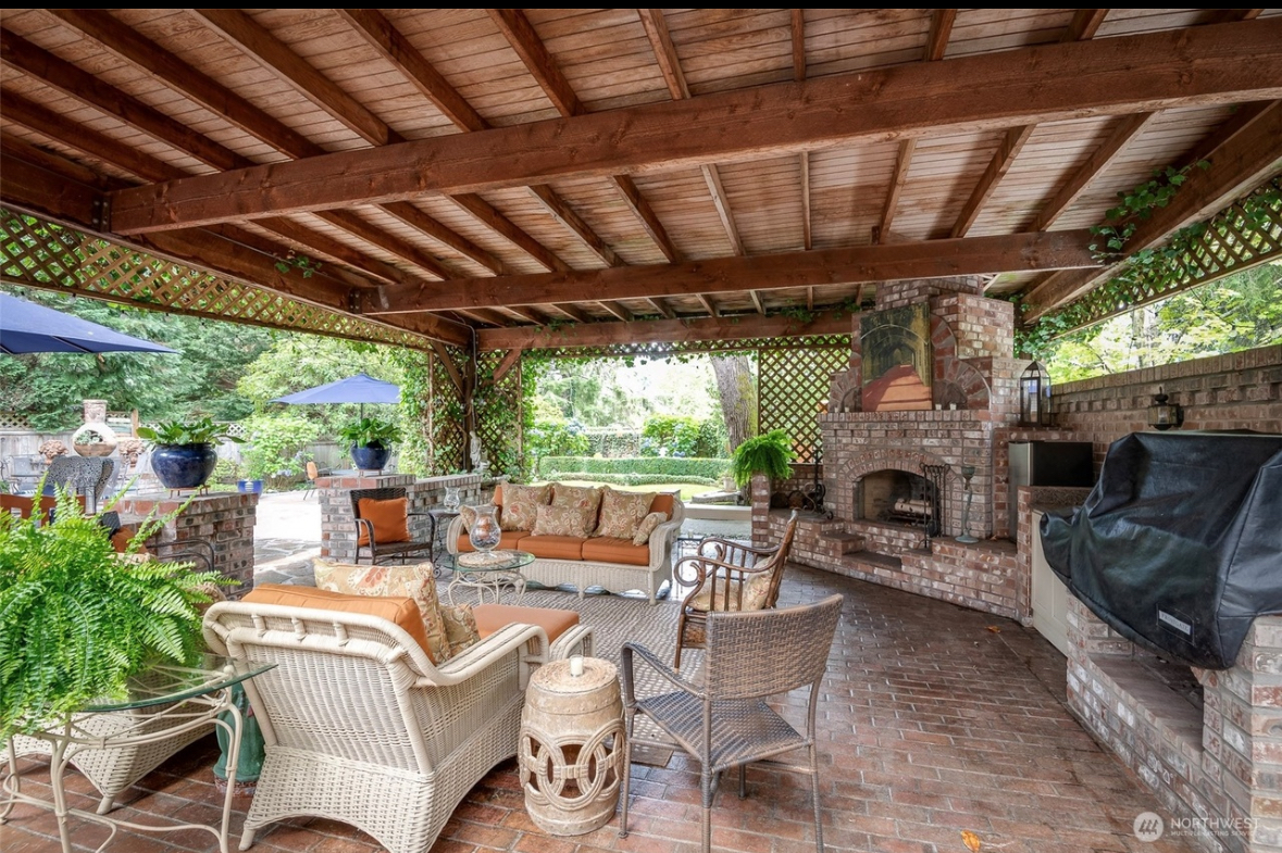 Covered back patio entertainment area with wicker seating, brick fireplace, and built-in grill